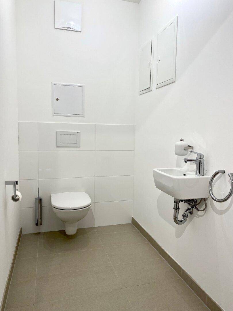 Modernes Gäste-WC mit Wand-WC, kleinem Waschbecken und hellen Fliesen in minimalistischem Design.