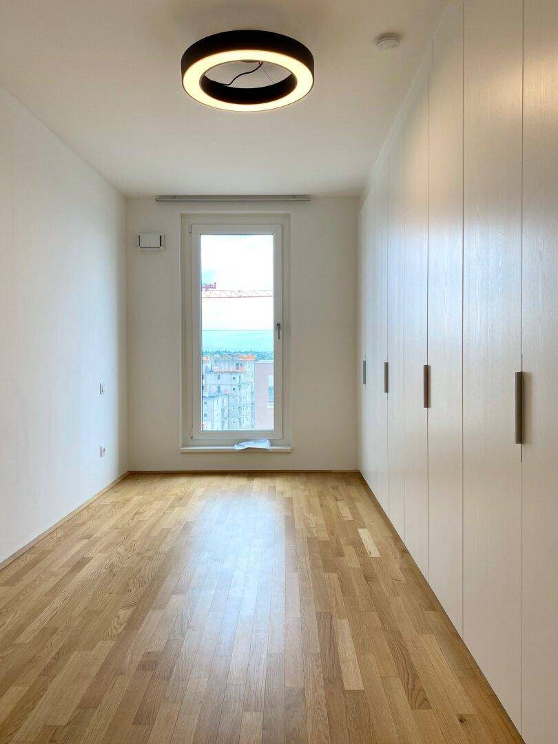 Helles Zimmer mit Holzboden, Einbauschränken und Fenster mit Ausblick.