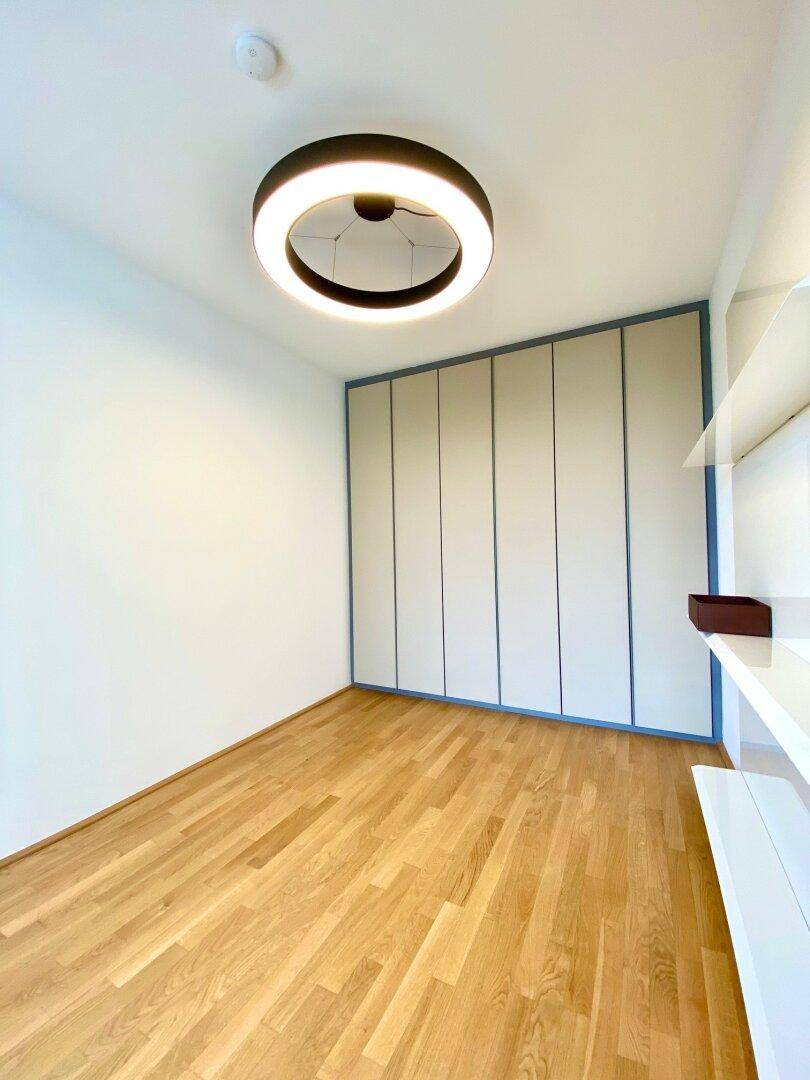Helles Zimmer mit Holzboden, Einbauschränken und moderner Deckenleuchte.
