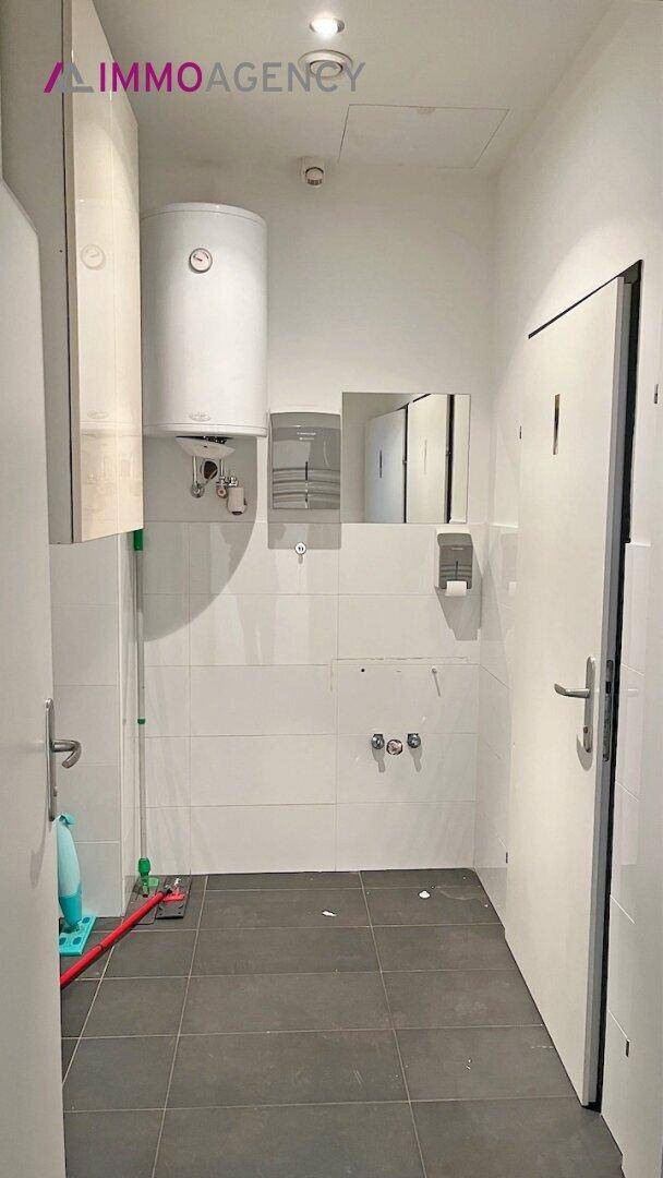 Einfacher Toilettenraum mit Boiler, Spiegel und Fliesenboden.