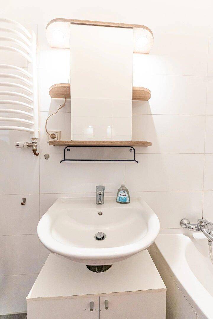 Waschbecken mit Spiegelschrank und Beleuchtung im hell gefliesten Badezimmer.