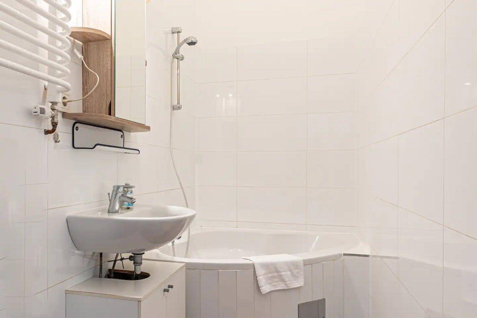 Badezimmer mit Badewanne, Duschkopf und weißer Fliesenverkleidung.