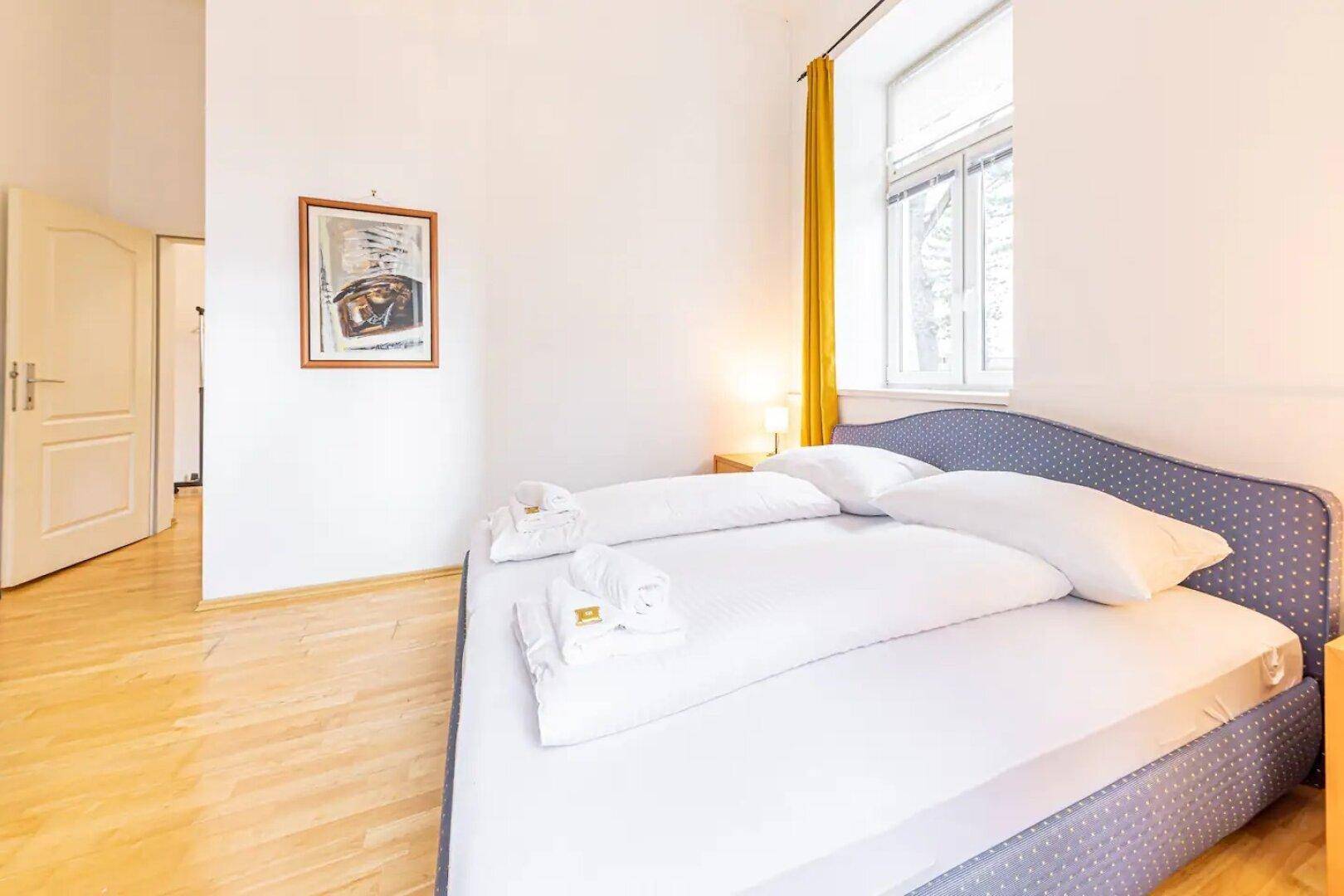 Schlafzimmer mit Doppelbett, Parkettboden und Zugang zu einem weiteren Raum.