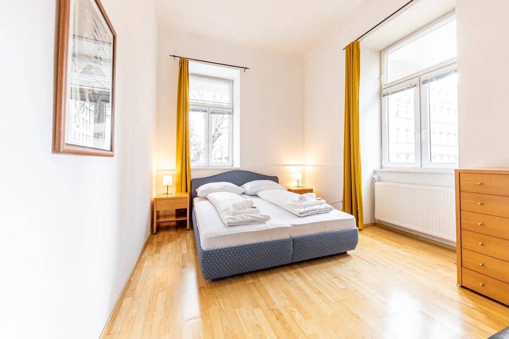 Schlafzimmer mit Doppelbett, Nachttischen und zwei großen Fenstern.