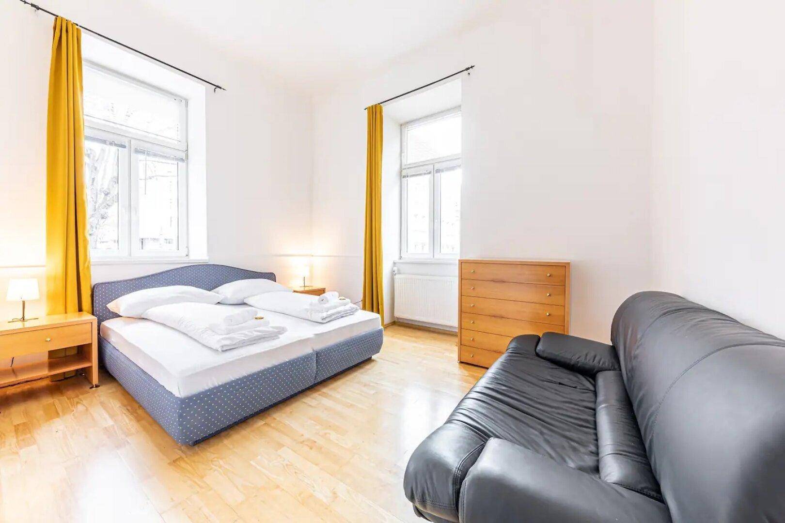 Helles Schlafzimmer mit Doppelbett, Kommode und einer zusätzlichen Sitzgelegenheit.