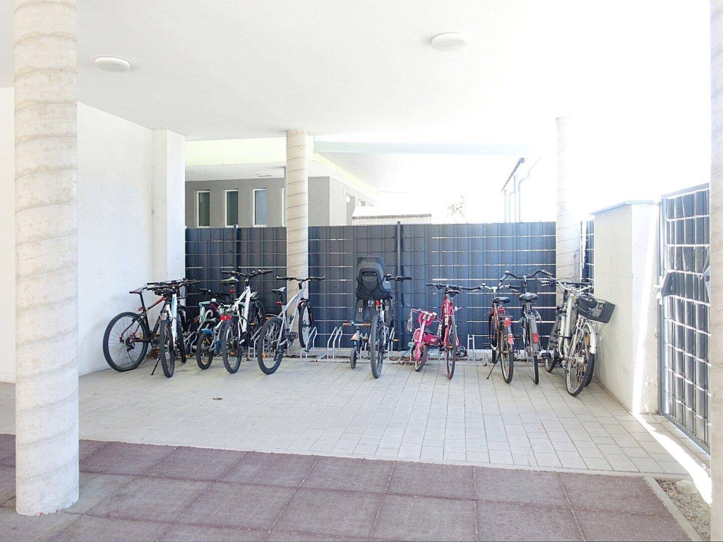 Überdachter Fahrradabstellplatz im Freien mit mehreren Fahrrädern und Säulen in einem gepflegten Bereich.