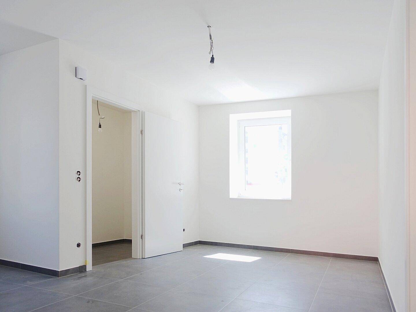 Lichtdurchfluteter Raum mit grauen Fliesen und einem Fenster, ideal für ein modernes Wohnkonzept.