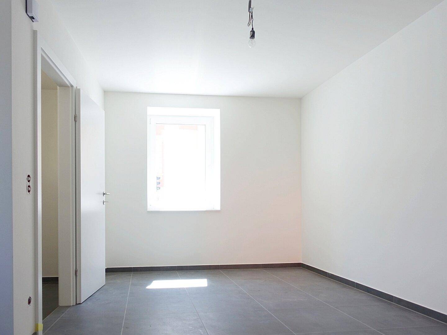 Helles Schlafzimmer mit grauen Fliesen und einem Fenster, das viel Sonnenlicht einfängt.