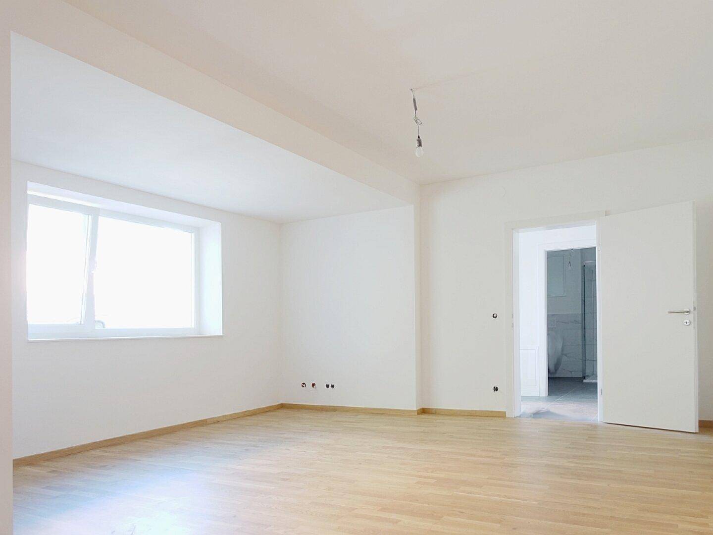 Heller Wohnraum mit neuem Parkettboden und großem Fenster, bereit für die individuelle Einrichtung.