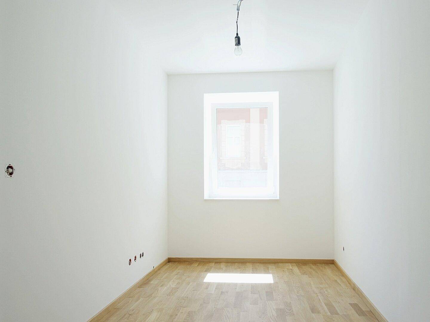Ruhiges Schlafzimmer mit hellem Parkettboden und einem Fenster, das viel Tageslicht hereinlässt.