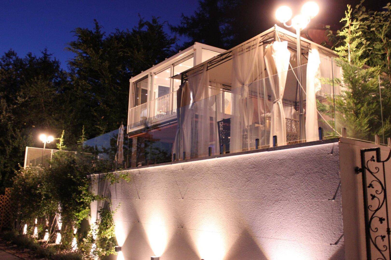 Beleuchtete Außenansicht des Hauses bei Nacht mit gläsernem Wintergarten und gemütlichem Pavillon.