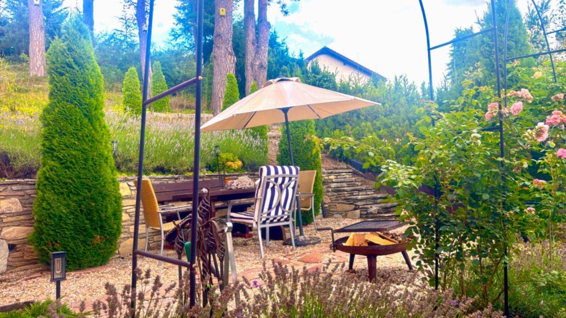 Idyllischer Gartenbereich mit Esstisch, Sonnenschirm und einer Feuerstelle für gemütliche Abende.
