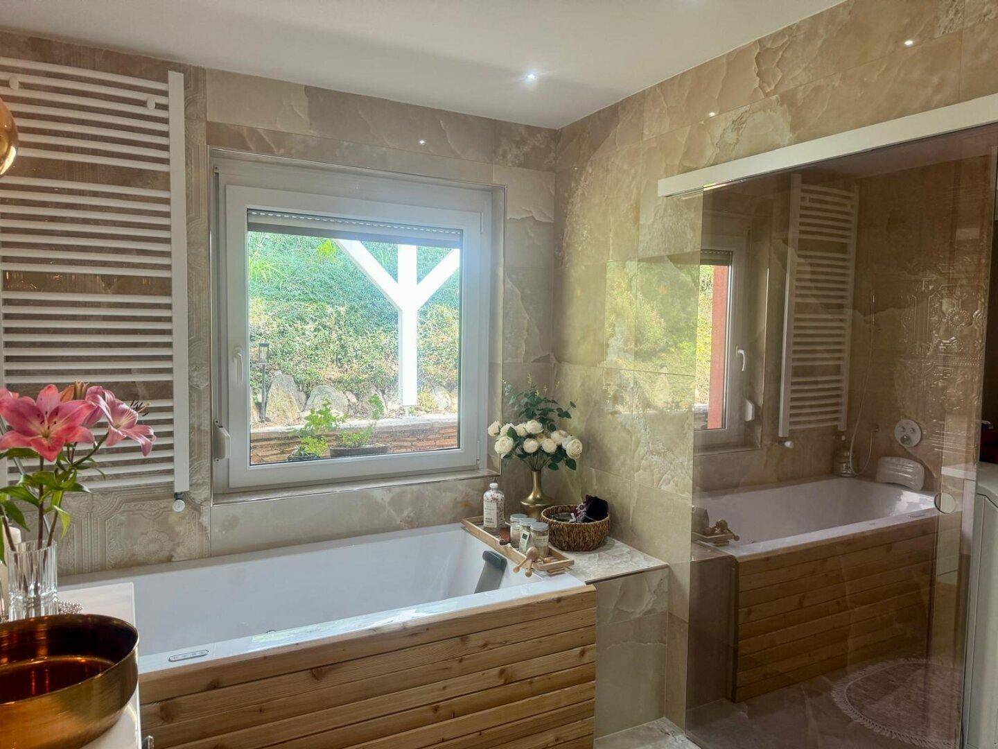 Modernes Badezimmer mit zwei Badewannen, Holzverkleidung und einem Fenster mit Grünblick.