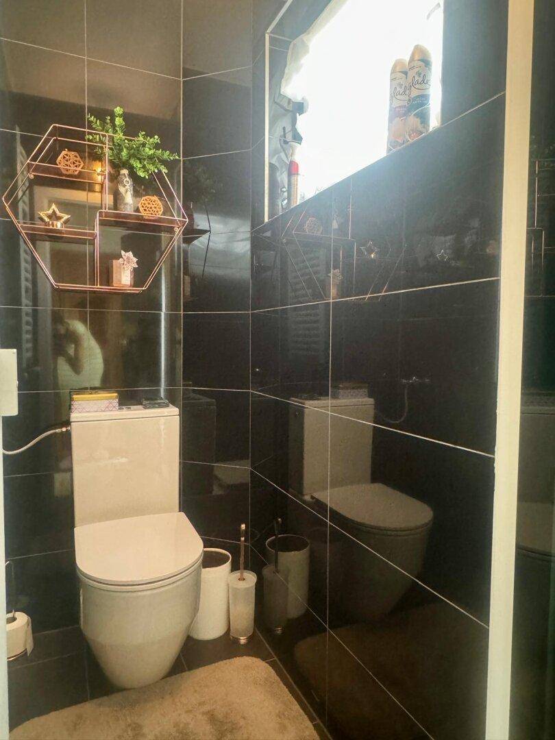 Kleines, modernes WC mit schwarzen Hochglanzfliesen und einem Fenster für Tageslicht.