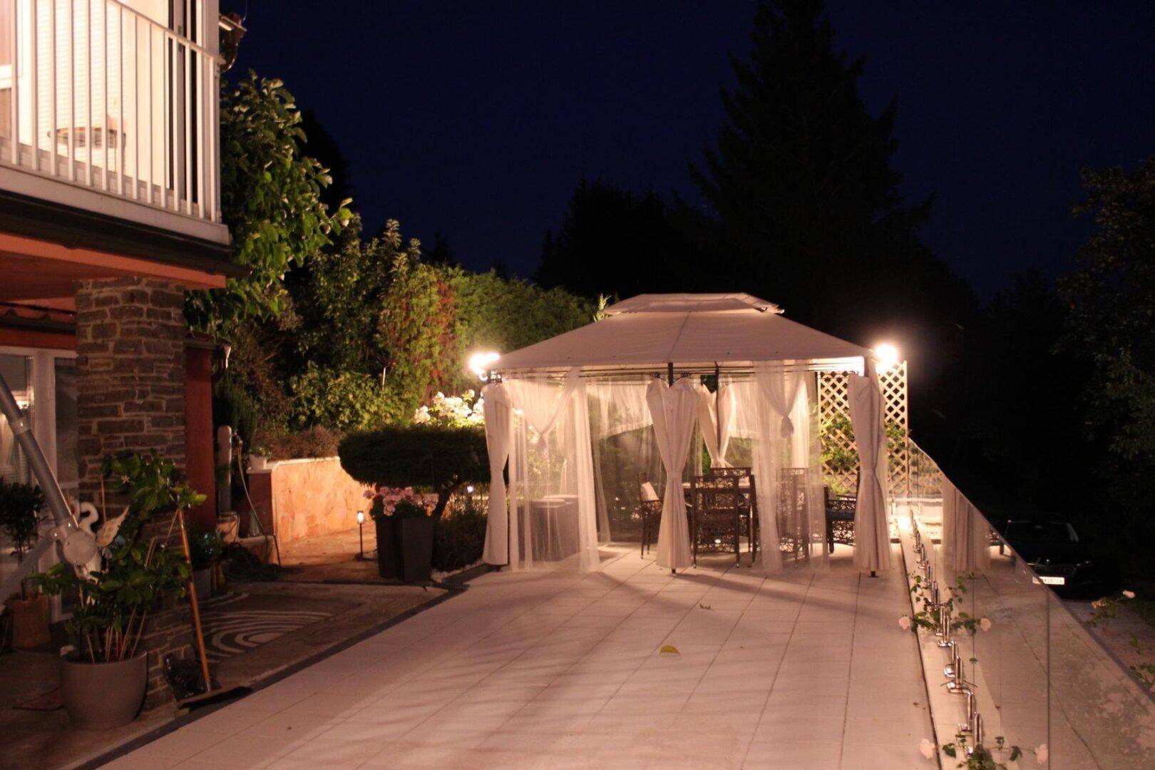 Beleuchtete Terrasse bei Nacht mit einem gemütlichen Pavillon und Zugang zum Haus.