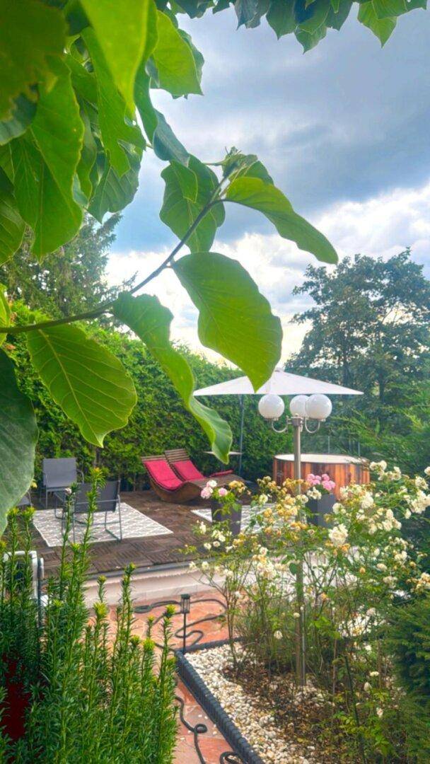 Entspannender Gartenbereich mit Whirlpool, Liegestühlen und üppiger grüner Bepflanzung.