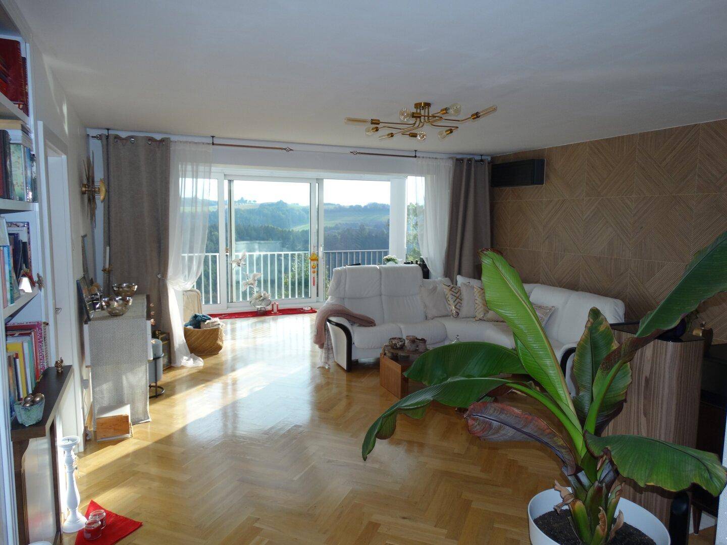 Helles Wohnzimmer mit Parkettboden, großen Fenstern und einem weiten Blick in die Natur.