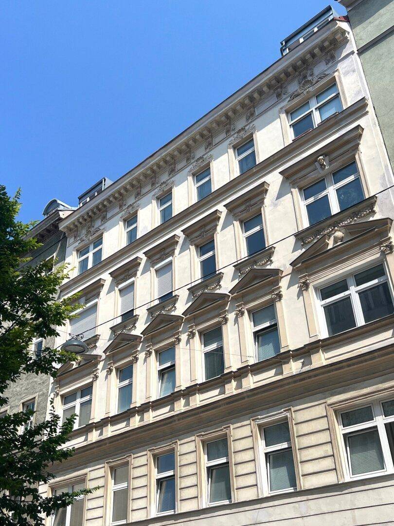 Klassische Altbaufassade mit dekorativen Elementen und vielen Fenstern unter blauem Himmel.