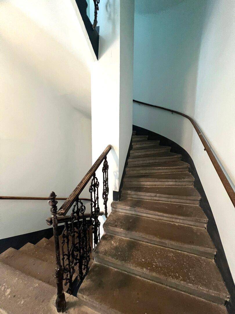 Historisches Treppenhaus mit geschwungenen Stufen und schmiedeeisernem Geländer.