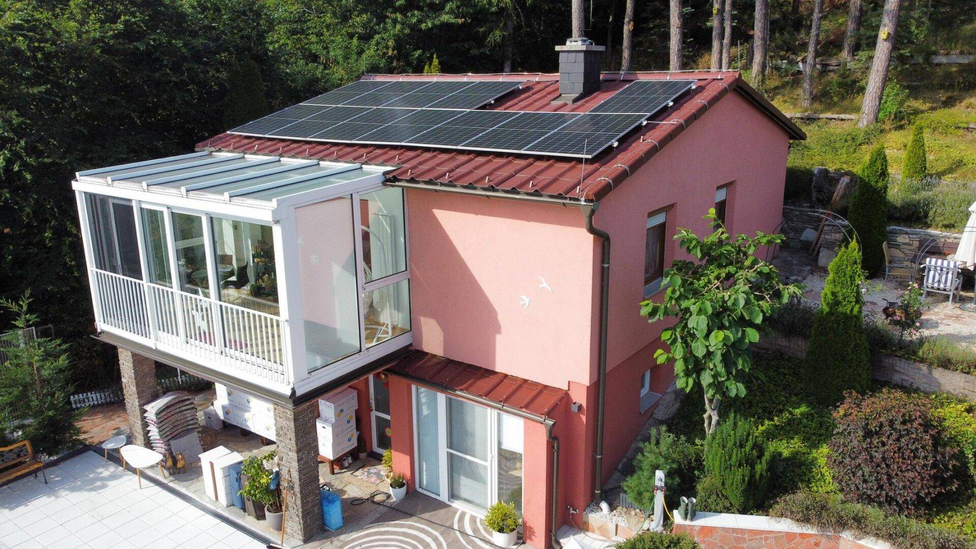 Das Haus von oben mit Solaranlage auf dem Ziegeldach und einem modernen Wintergarten.