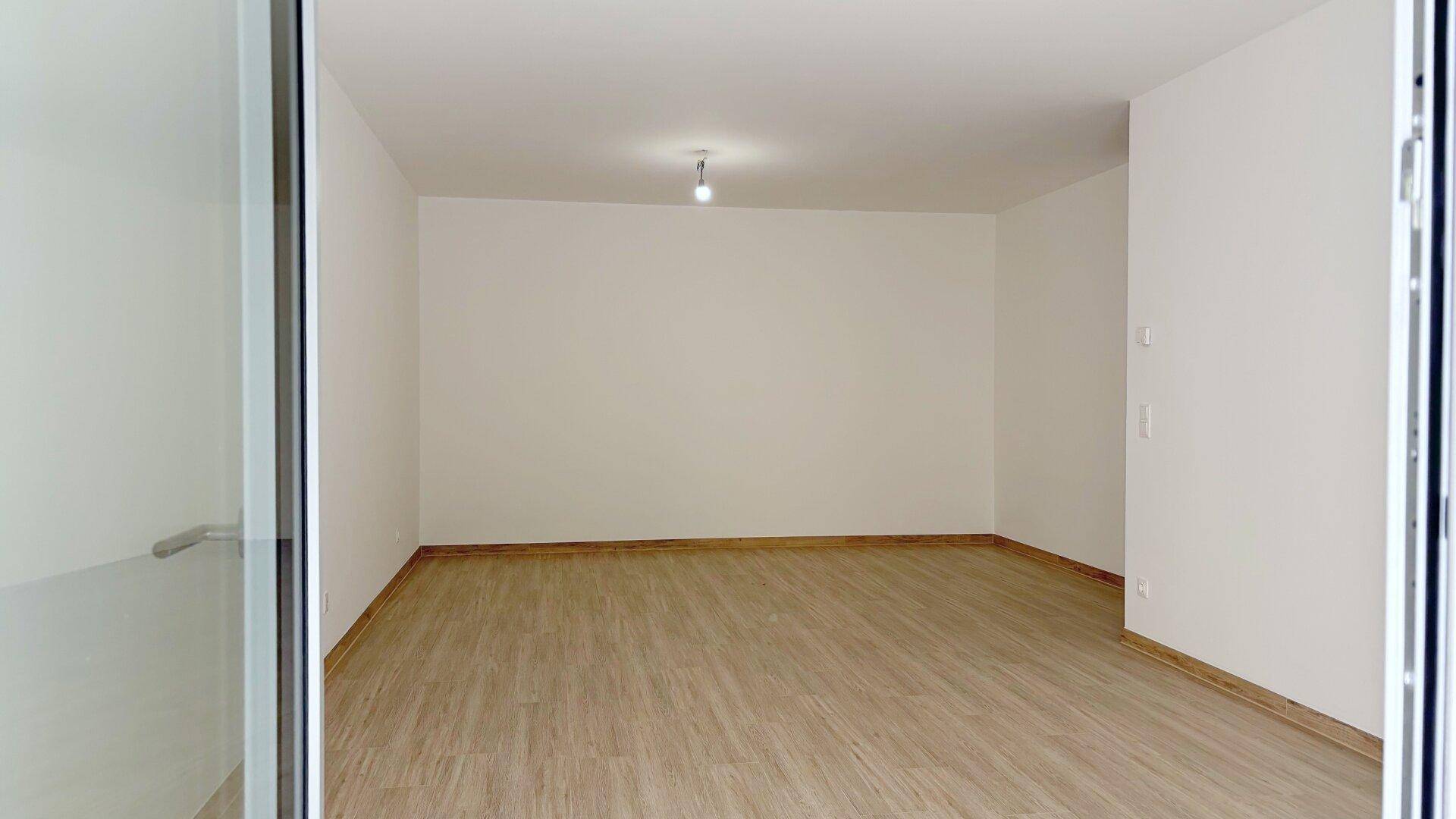 Heller, leerer Raum mit modernem Bodenbelag und einer großen Fensterfront, die viel Tageslicht hereinlässt.