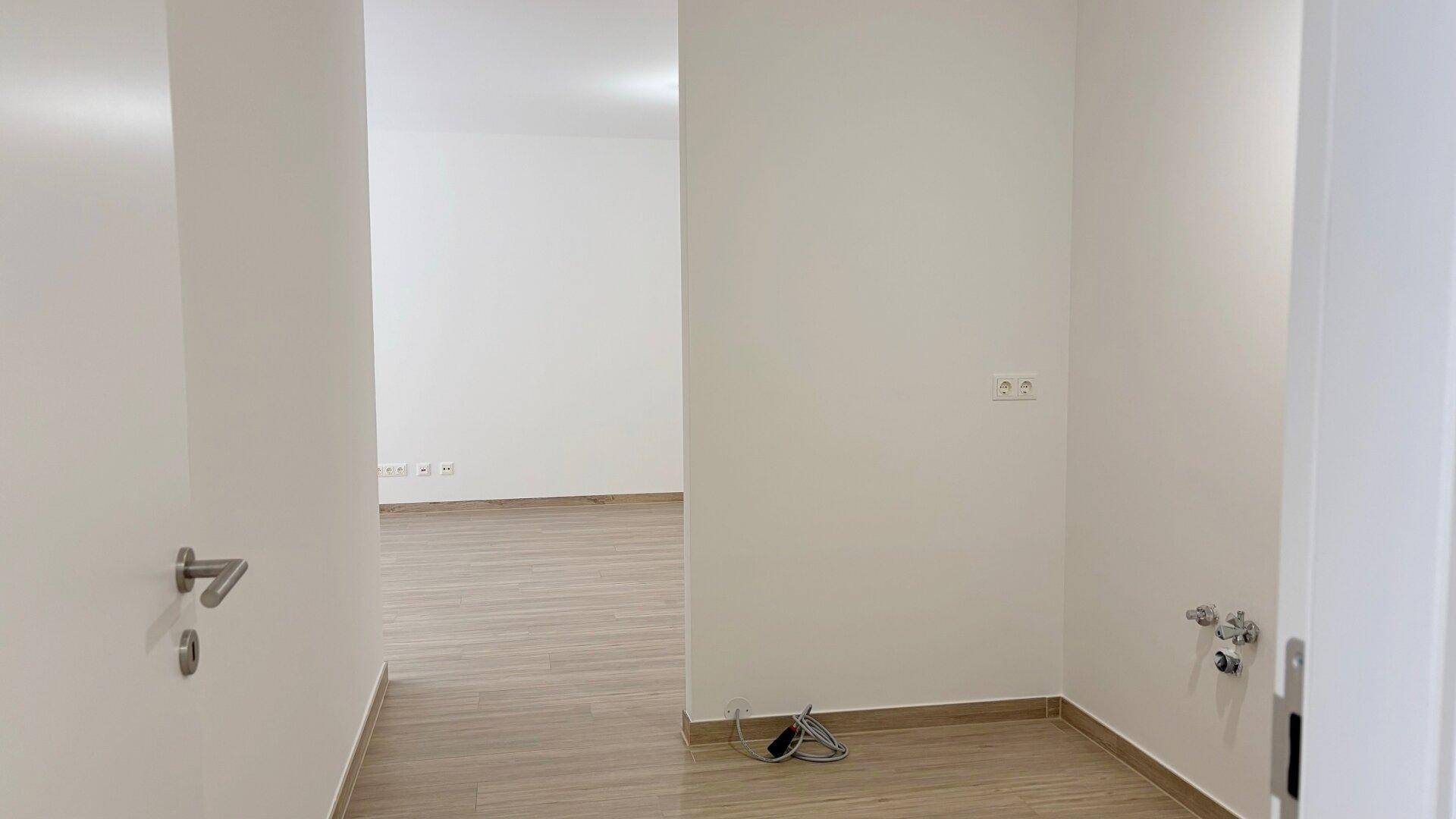 Flur oder Übergangsbereich mit hellem Bodenbelag und sichtbaren Anschlüssen an der Wand.