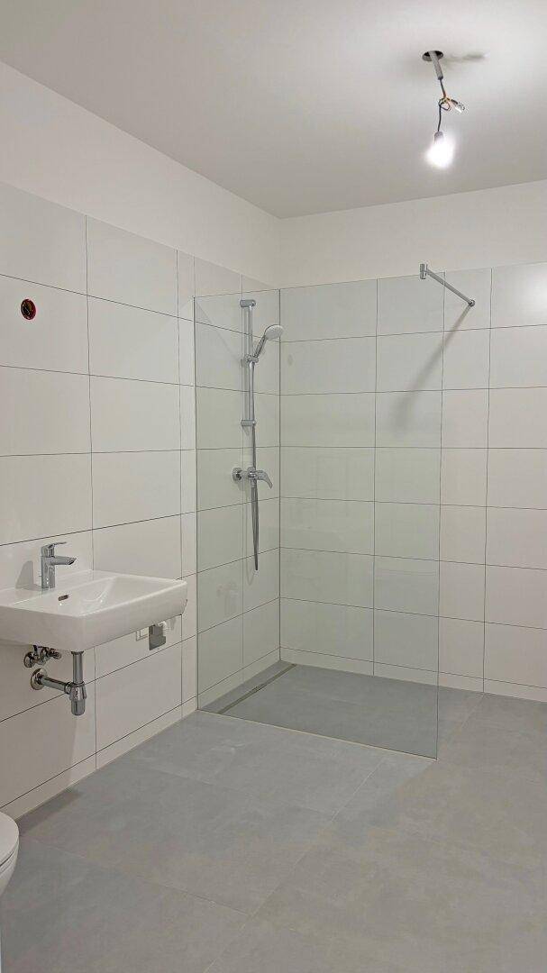 Modernes Badezimmer mit weißen Wandfliesen, grauen Bodenfliesen und einer begehbaren Dusche mit Glaswand.
