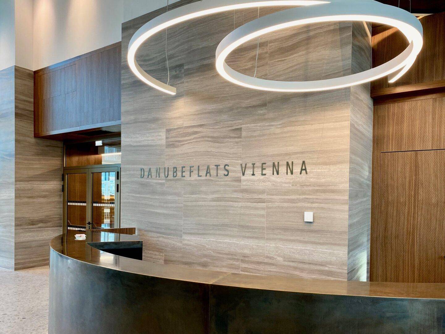 Moderner Empfangsbereich mit stilvoller Beleuchtung, Marmorwänden und dem Schriftzug "DANUBEFLATS VIENNA".