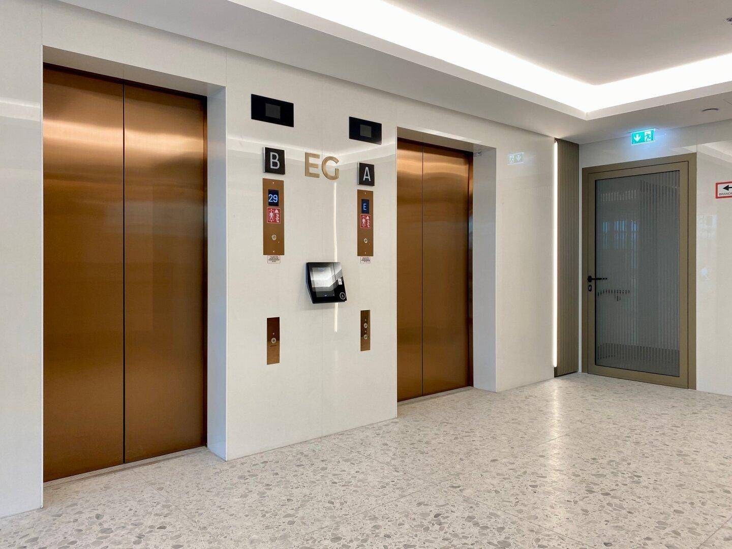 Moderner Aufzugsbereich mit eleganten Bronzetüren und digitaler Anzeige in einem luxuriösen Gebäude.