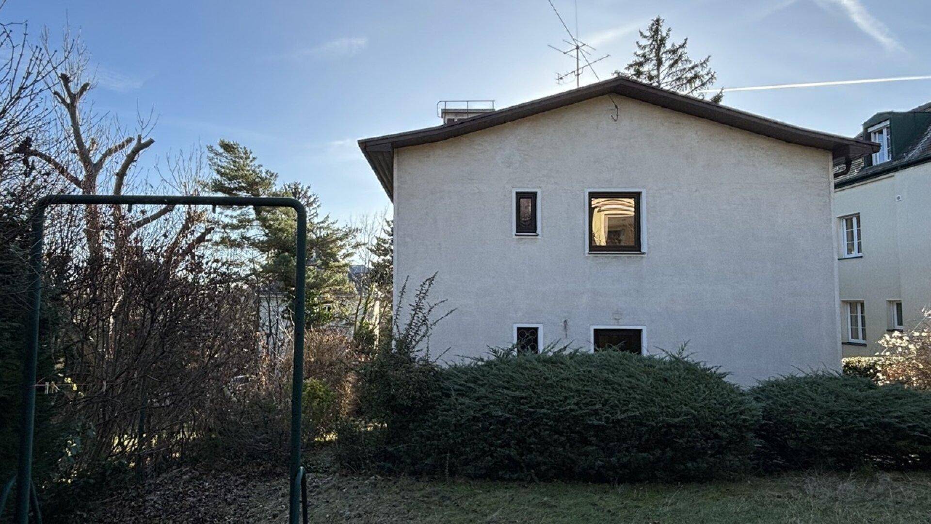 Gartenansicht des Hauses mit einem Schaukelgestell und Bäumen unter klarem Himmel.