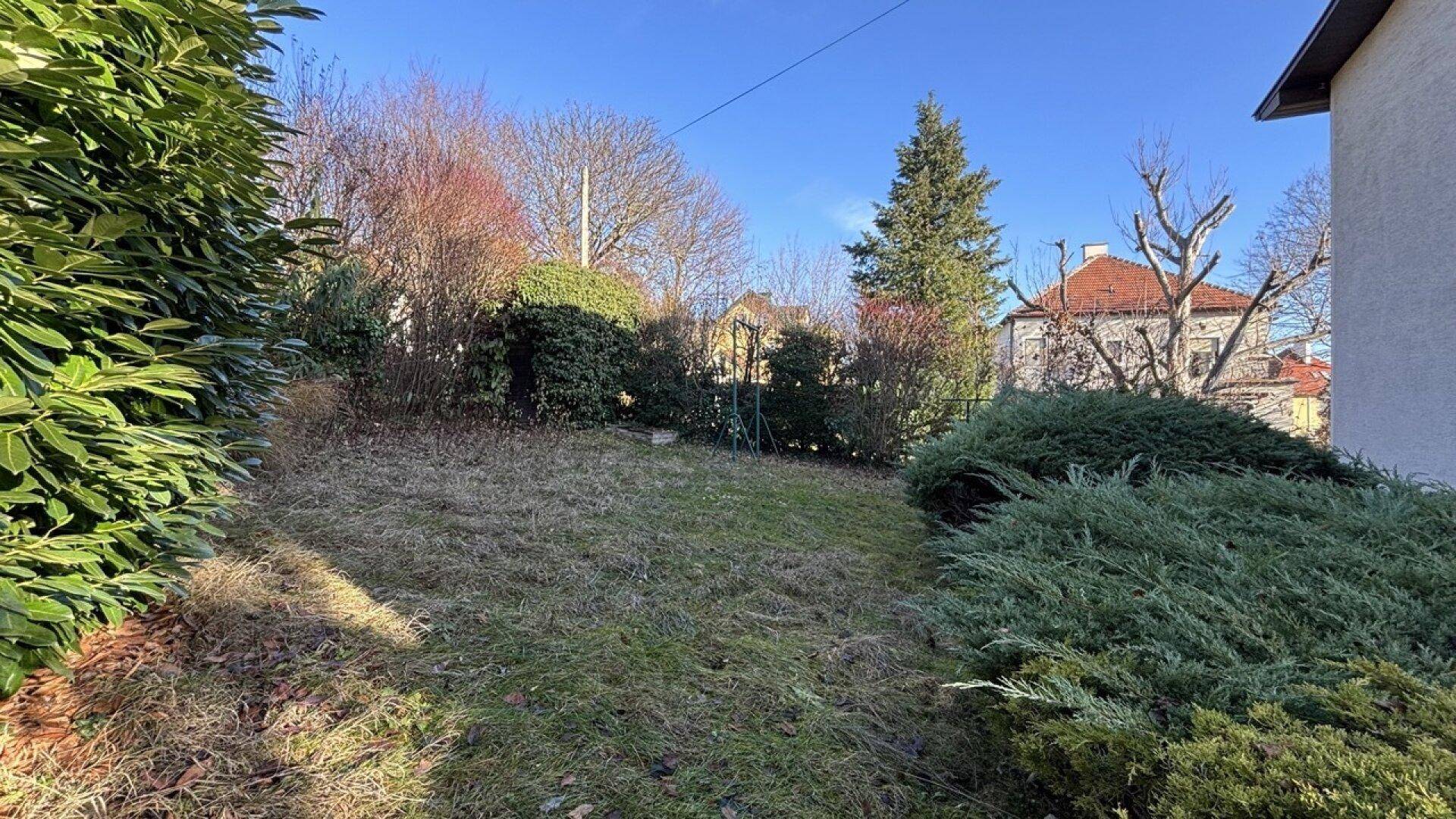 Weitläufiger Gartenbereich mit Rasen, Sträuchern und Blick auf die umliegenden Häuser.