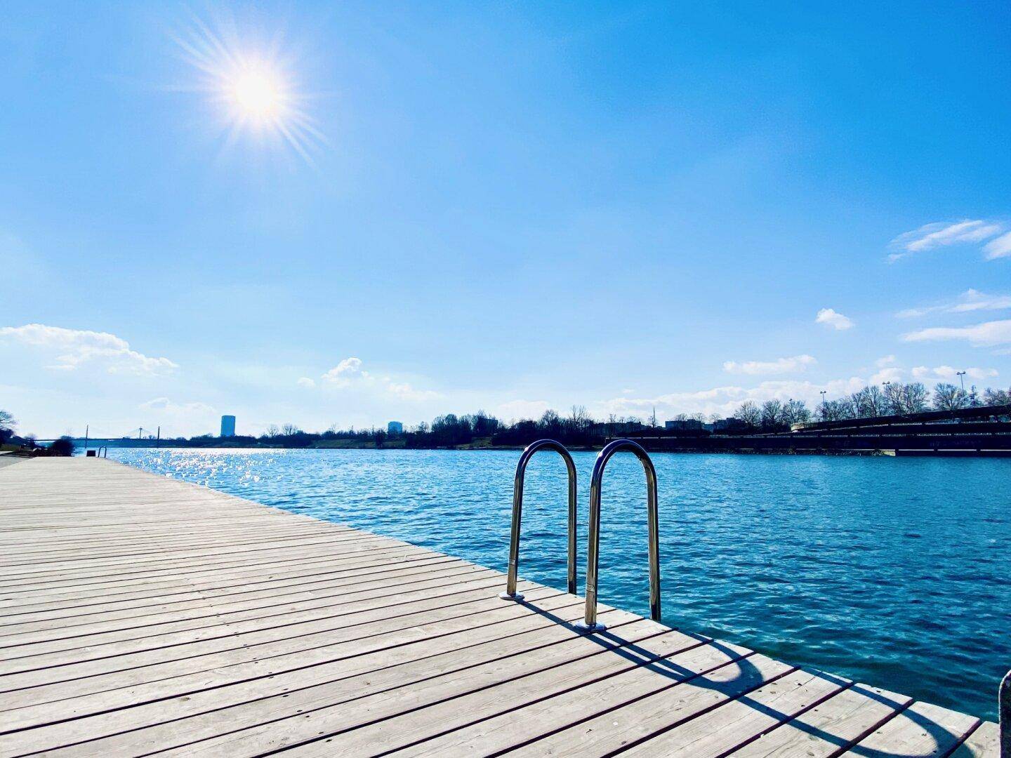 Holzsteg am Flussufer unter strahlend blauem Himmel, ideal für entspannte Stunden am Wasser.
