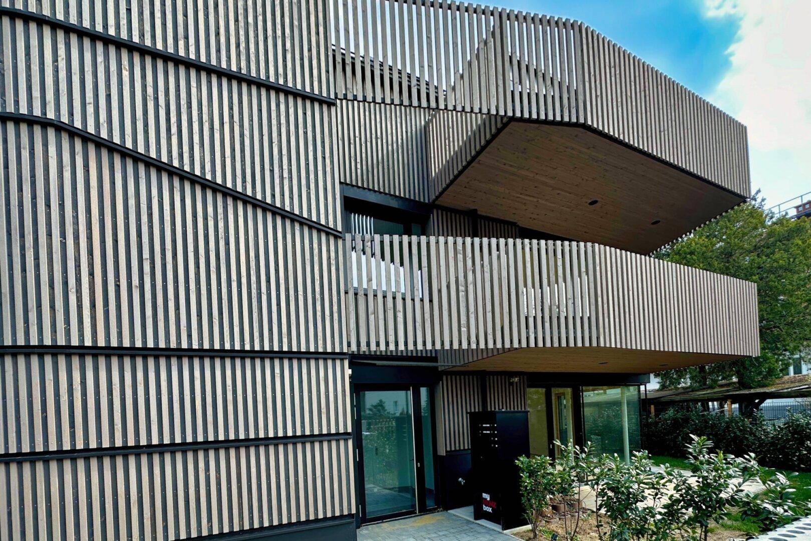 Detailansicht der modernen Holzlamellenfassade und der Balkone des Gebäudes.