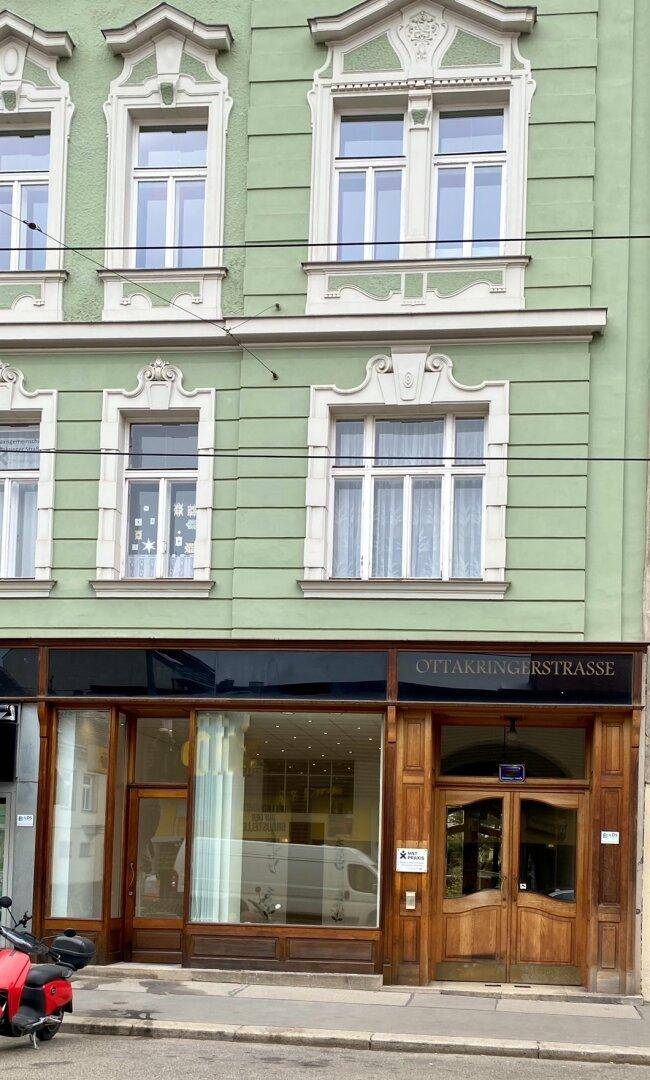 Grüne Fassade eines Altbaus mit dekorativen Fenstern und dem Ladenlokal im Erdgeschoss.