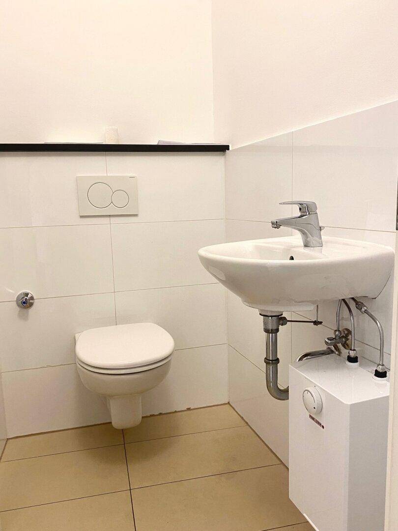 Modernes Gäste-WC mit wandhängender Toilette, Waschbecken und weiß gefliesten Wänden.