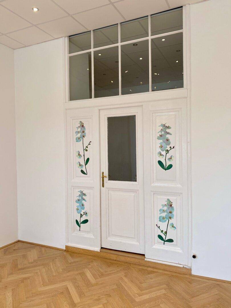 Dekorative weiße Türen mit floralen Mustern und einem großen Oberlicht, das Licht hereinlässt.