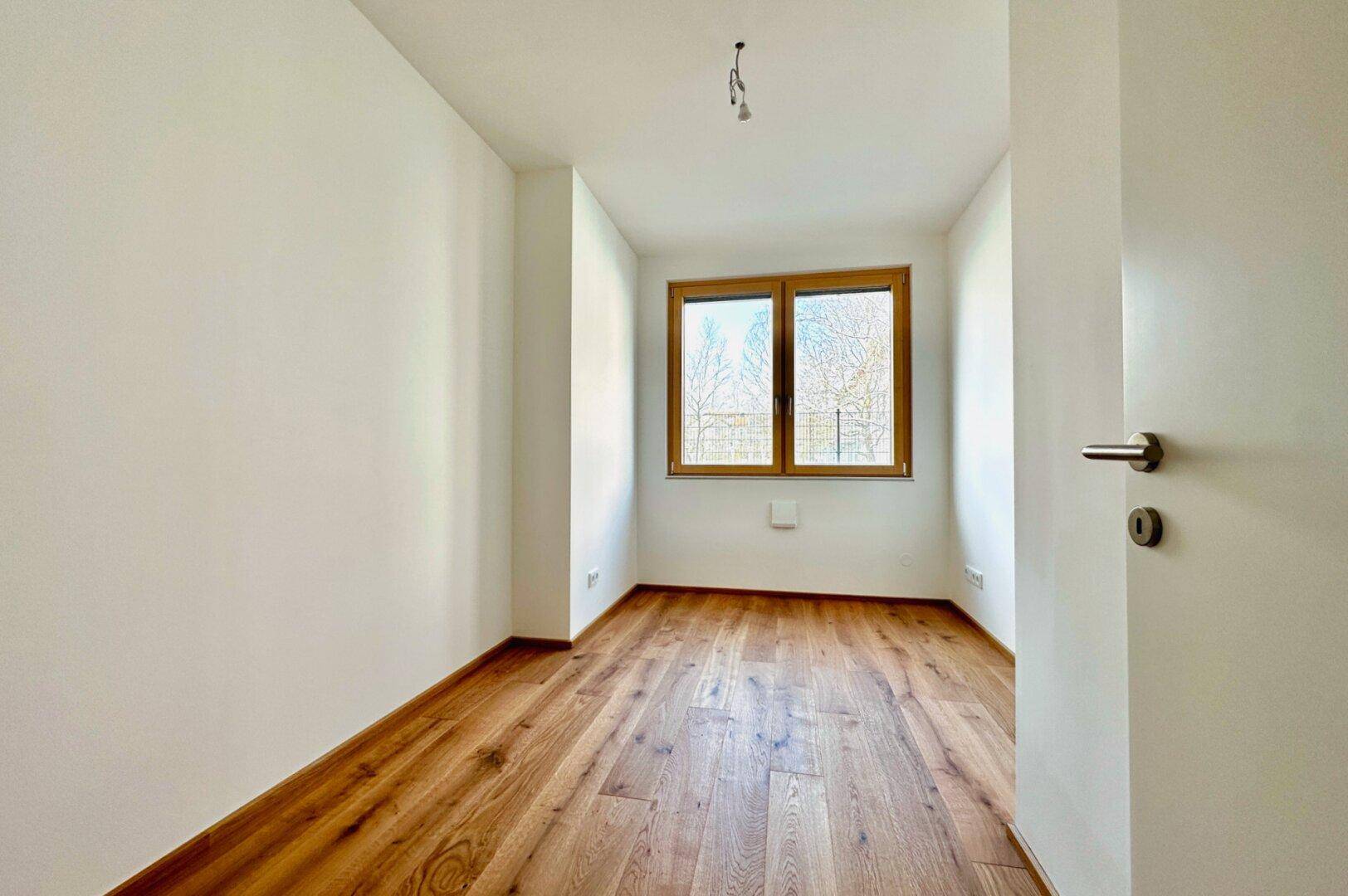 Helles, leeres Schlafzimmer mit Holzboden und Fenster, ideal für ein Kinderzimmer oder Büro.