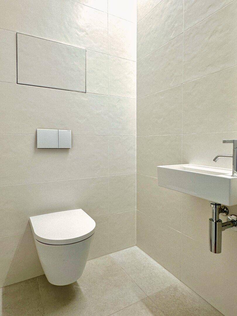 Modernes Gäste-WC mit wandhängender Toilette und kleinem Waschbecken, komplett gefliest.