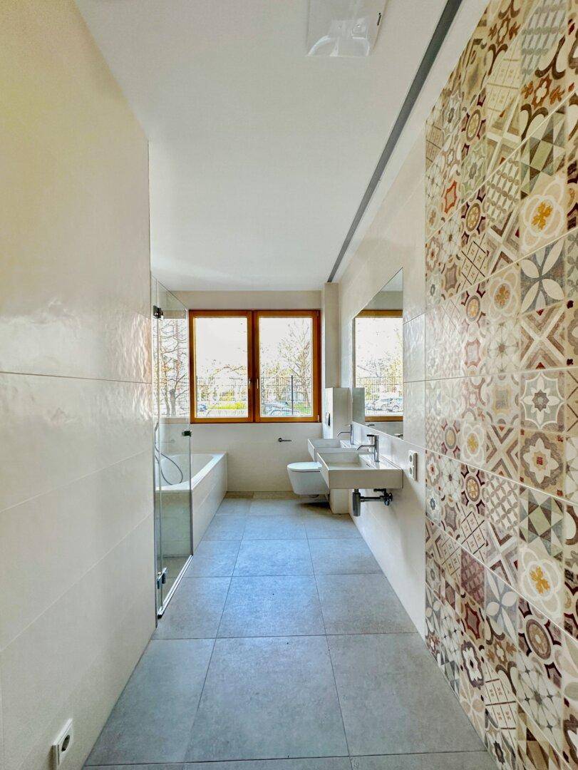 Modernes Badezimmer mit Badewanne, Dusche, Doppelwaschbecken und dekorativen Fliesen.