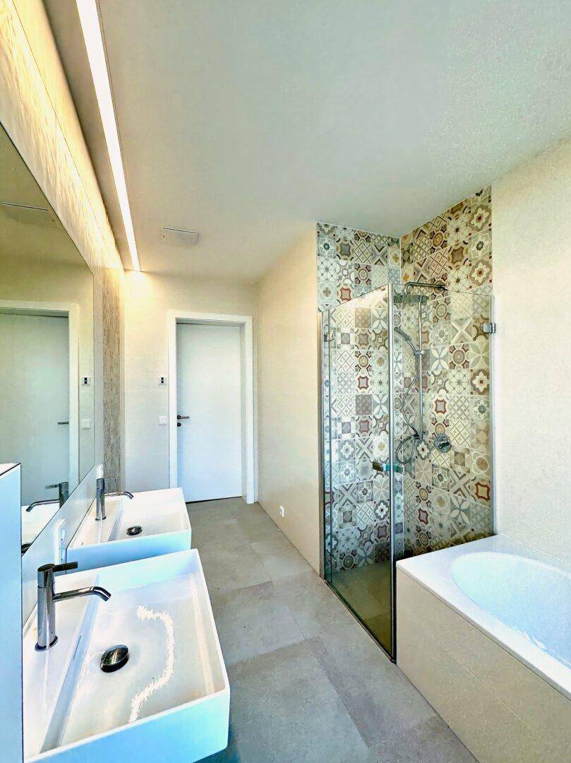 Elegantes Badezimmer mit begehbarer Dusche, Doppelwaschbecken und gemusterten Wandfliesen.