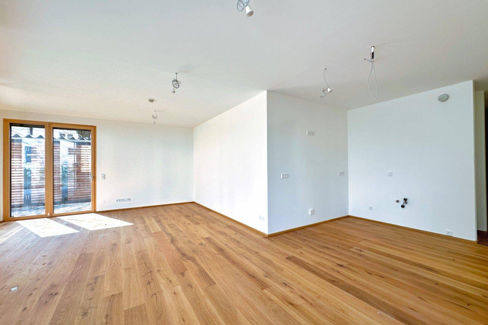 Geräumiges, helles Wohnzimmer mit Holzboden und weißen Wänden, bereit zur Einrichtung.