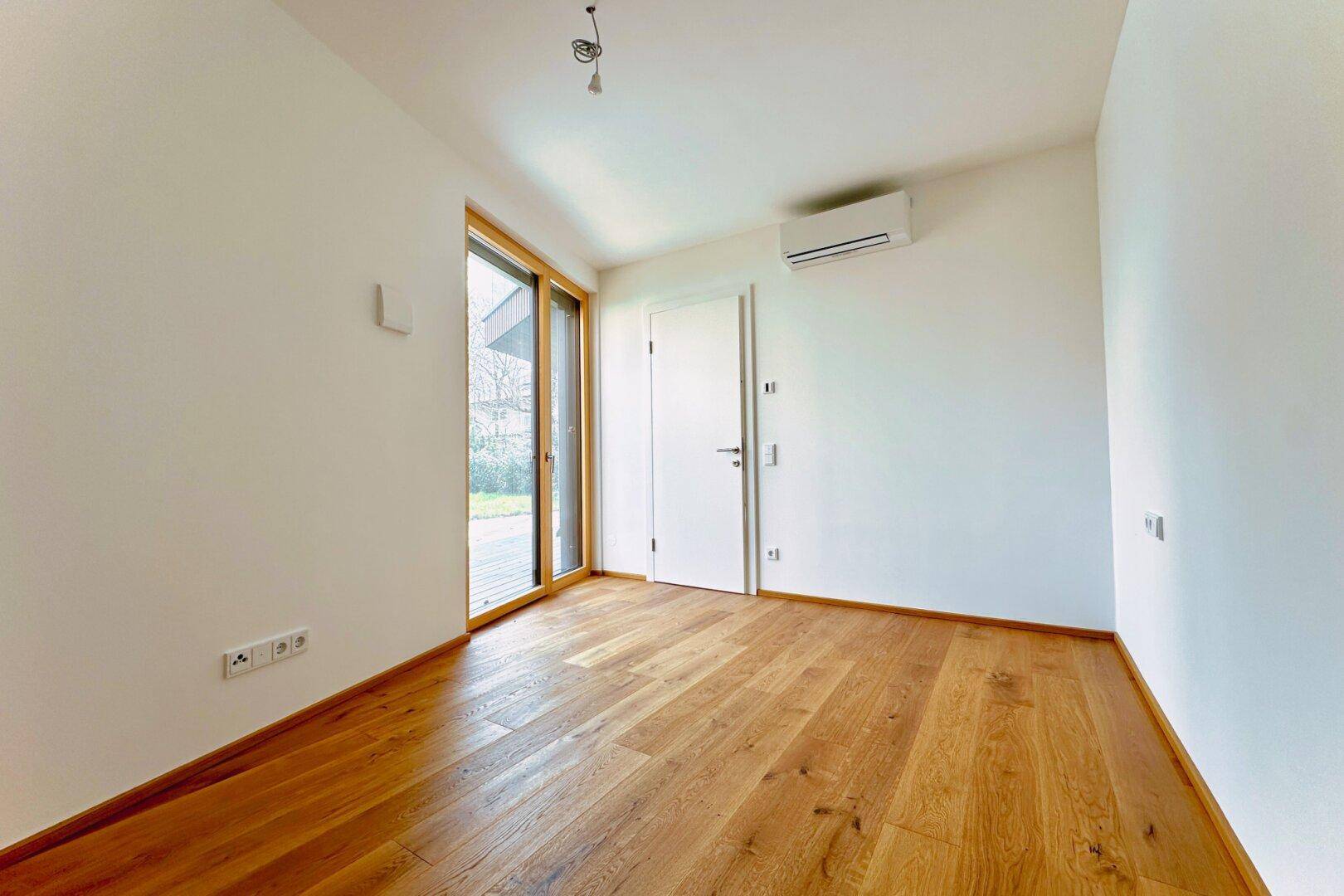 Geräumiges Schlafzimmer mit Holzboden, Klimaanlage und Zugang zur Terrasse oder zum Garten.