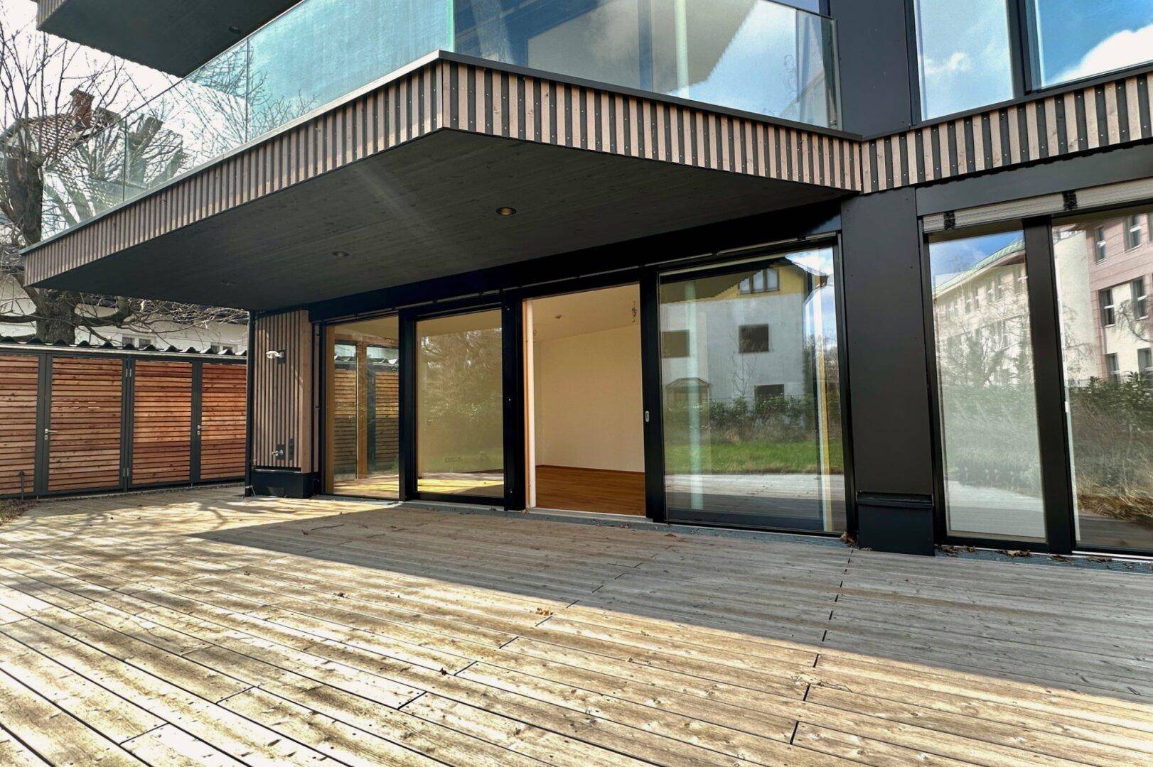 Große Holzterrasse vor dem modernen Gebäude mit Zugang zu den Innenräumen.