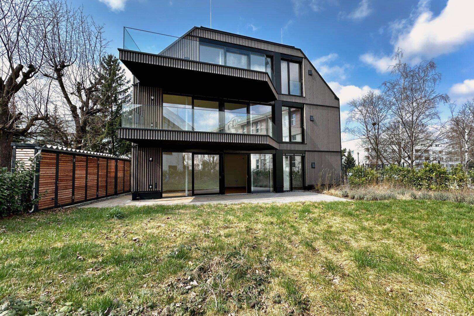 Modernes Wohngebäude mit Holzfassade und großzügiger Rasenfläche im Vordergrund.