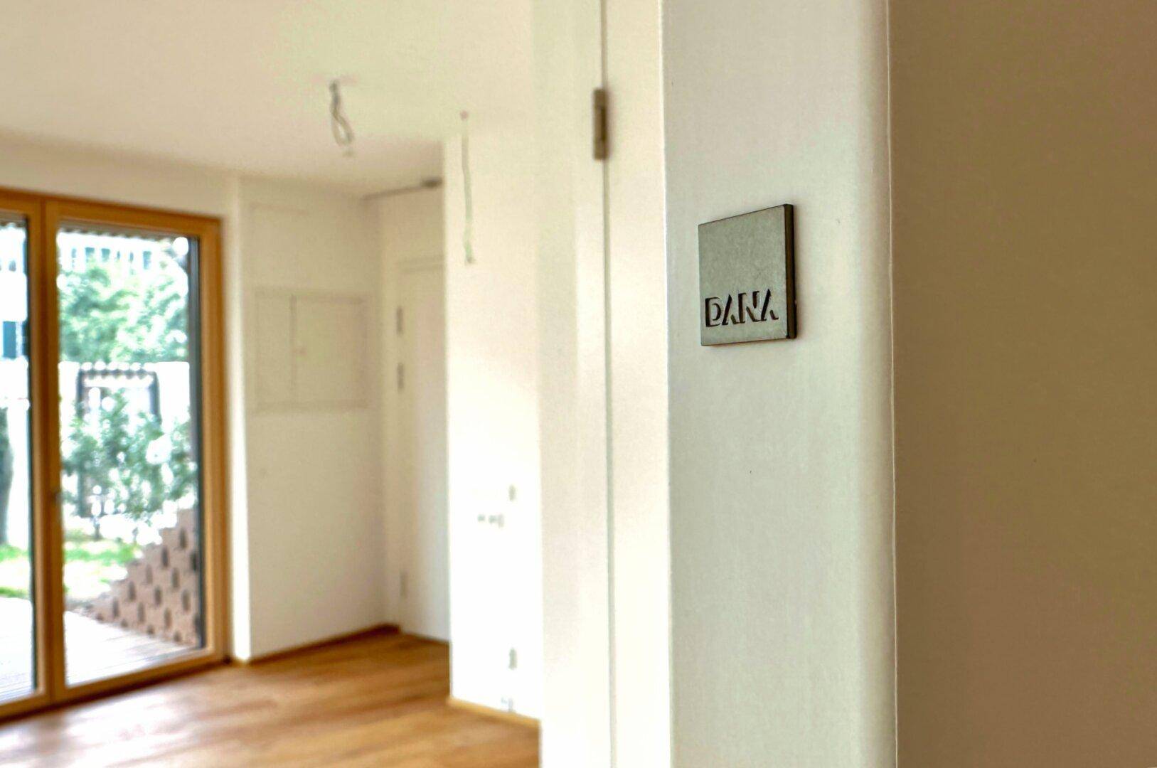 Nahaufnahme einer weißen Wand mit einem kleinen, modernen Schild mit der Aufschrift 'DARA'.