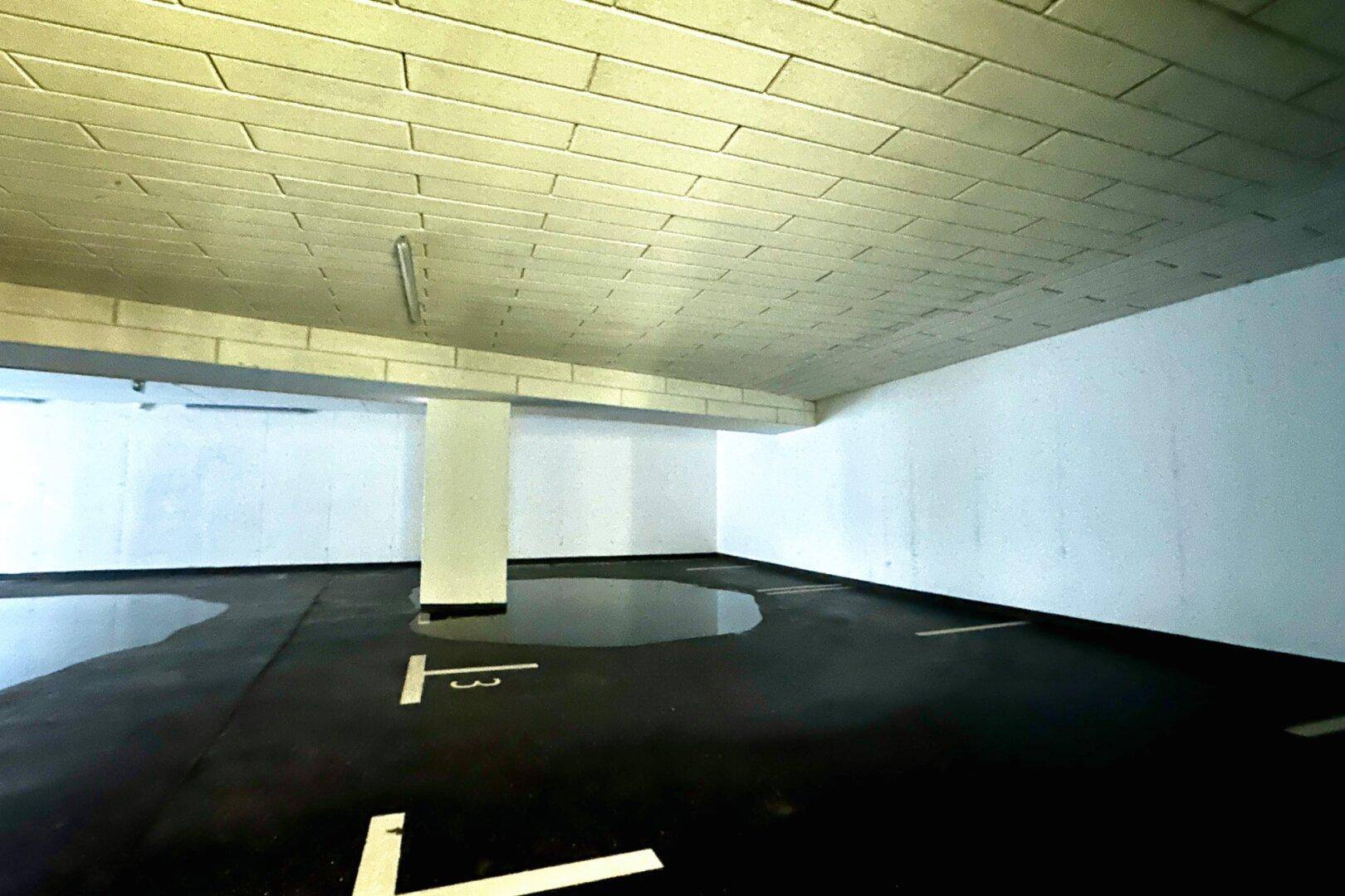 Leere Tiefgarage mit Betonboden, Parkmarkierungen und einigen Wasserpfützen.