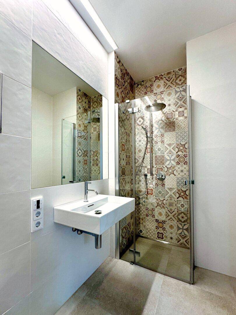 Stilvolles Badezimmer mit modernen Armaturen, Einzelwaschbecken und einer begehbaren Dusche mit gemusterten Fliesen.