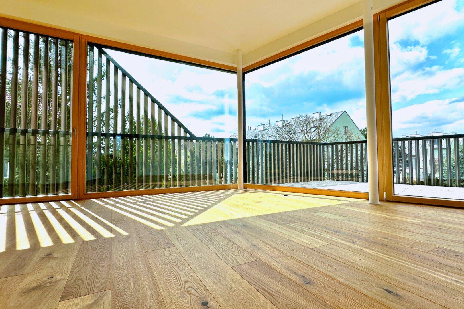 Heller Wohnraum mit Eichenparkett und raumhohen Fenstern, die Zugang zu einem Balkon bieten.