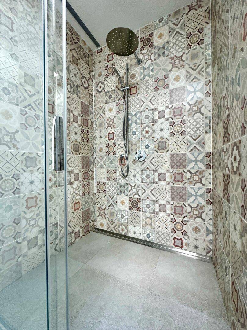 Duschbereich im modernen Badezimmer mit Regendusche und auffälligen, gemusterten Wandfliesen.