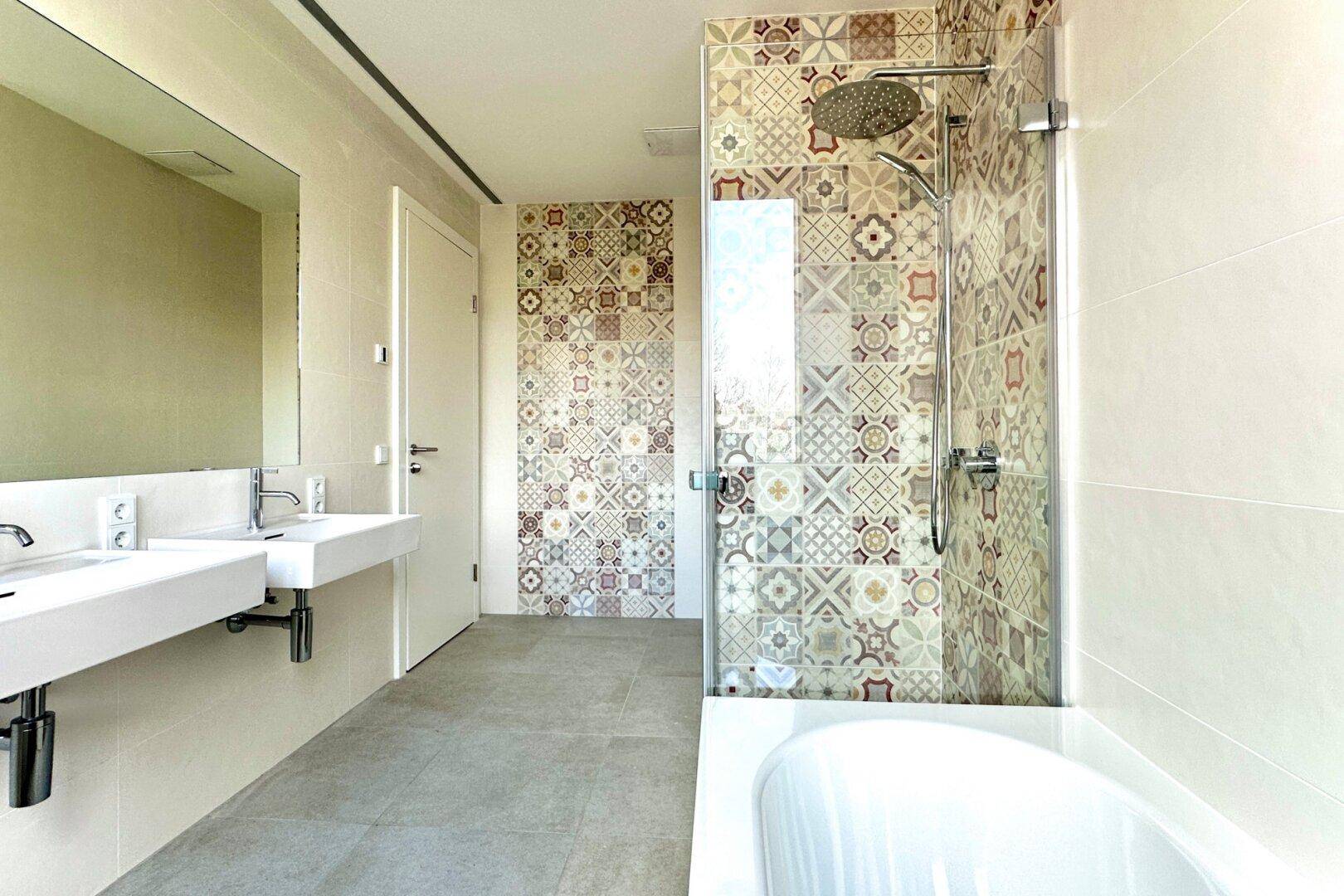 Geräumiges Badezimmer mit zwei Waschbecken, Badewanne und Duschbereich mit dekorativen Fliesen.